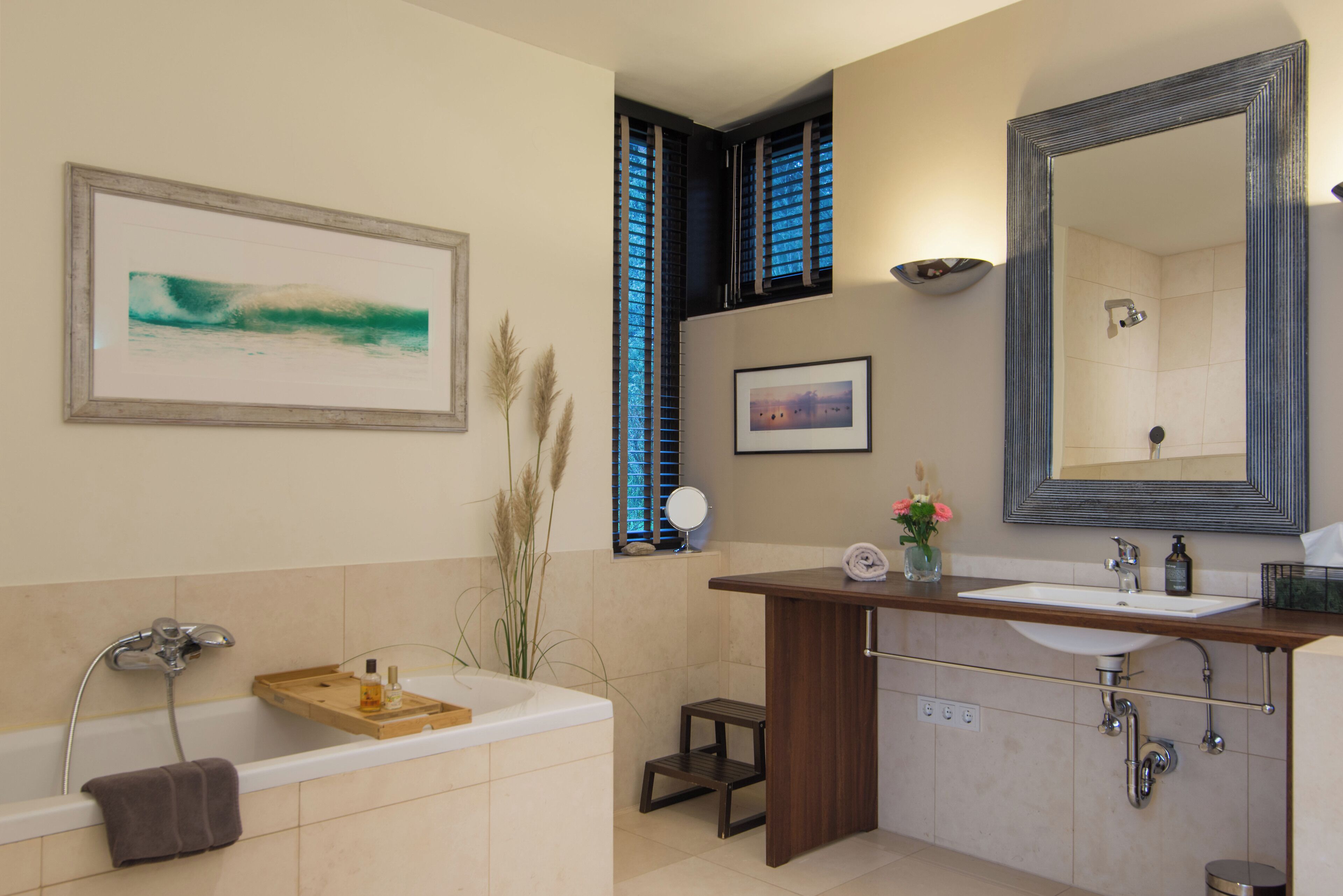 Un baño moderno con una bañera, un tocador de madera, un espejo grande y obras de arte enmarcadas en las paredes.