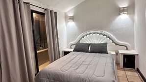 Une chambre à coucher avec un grand lit, une table de chevet, une lampe fixée au mur et une porte coulissante.