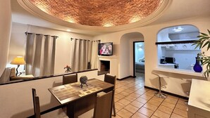 Un coin repas avec un plafond en briques, un téléviseur et une cuisine en arrière-plan.