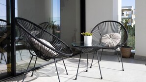 Ein Balkon mit zwei schwarzen Stühlen aus Draht, einem kleinen Tisch und einem Blumentopf.