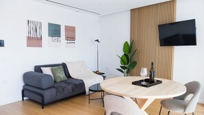 Ein modernes Wohnzimmer mit einem grauen Sofa, einem runden Holztisch und einem an der Wand befestigten Flachbildfernseher.
