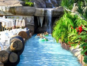 A water slide with people on tubes, surrounded by lounge chairs and umbrellas.