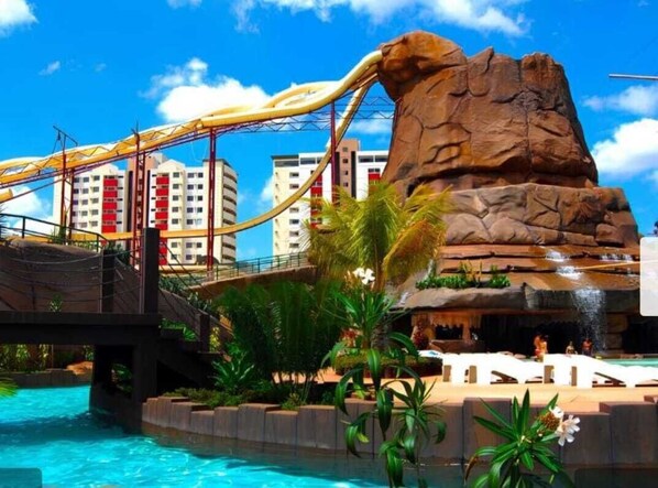 A water park with a large rock formation, a bridge, and a pool.