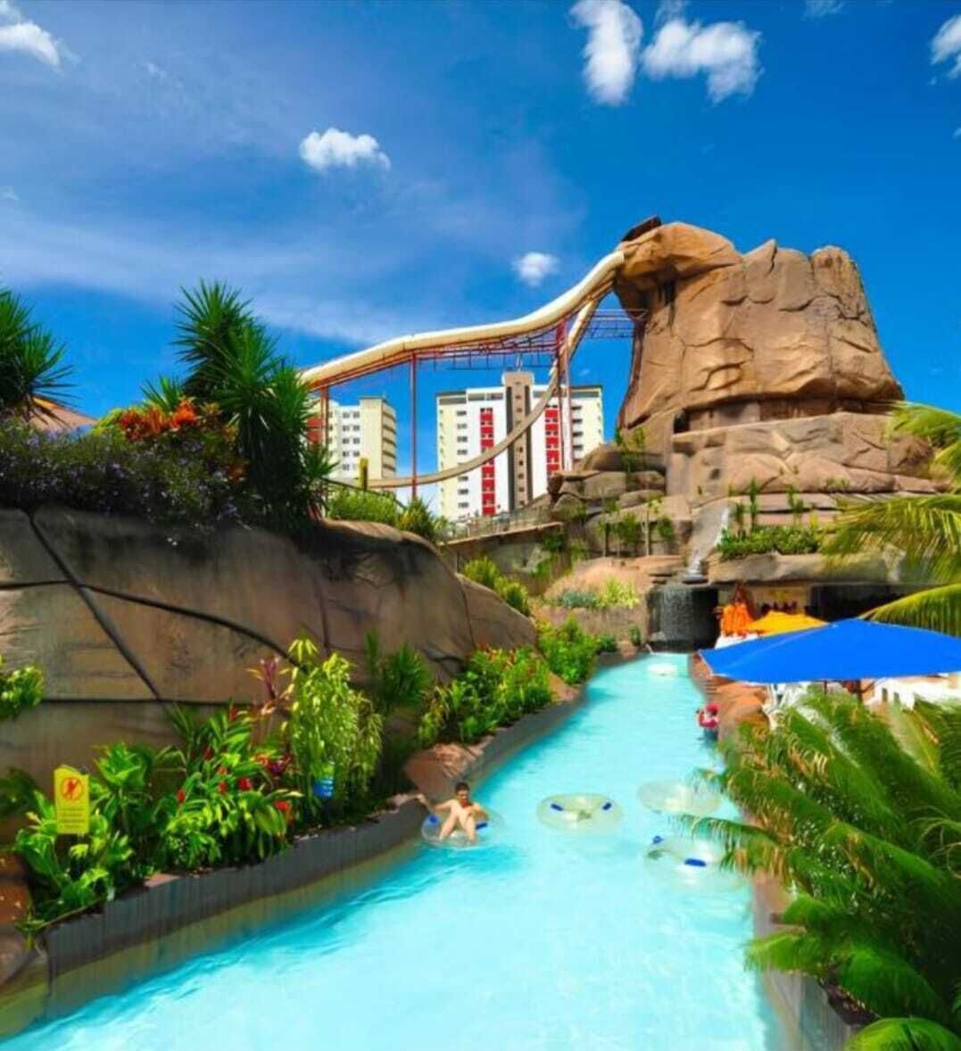 A water park with a large pool, a water slide, and a rocky landscape.