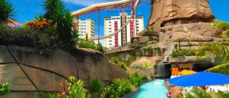 A water park with a large pool, a water slide, and a rocky landscape.