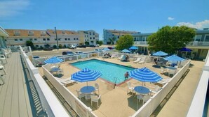 A rooftop pool area with lounge chairs and umbrellas, surrounded by a white fence.