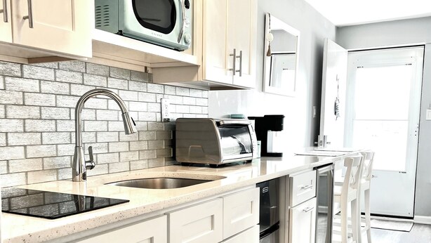 A modern kitchen with white cabinets, a stainless steel sink, a microwave, a toaster, and a dishwasher.