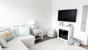 Una sala de estar moderna con un sofá blanco, un televisor de pantalla plana, una chimenea y un letrero que dice 'WELCOME'.