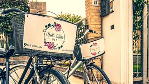 Deux vélos équipés de paniers portant l’inscription « Villa Lilla B&B » sont garés devant un immeuble.