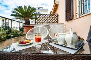 Un balcon avec une table préparée pour le petit-déjeuner, comprenant une assiette de nourriture, un verre de jus et des pichets en céramique blanche.