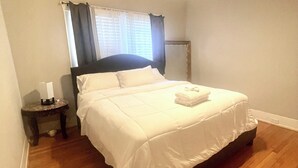 A neatly made bed in a room with wooden flooring, a small bedside table, and a ceiling fan. - Magic City Home walkable to Top Golf, New Amphitheater, Uptown, City Walk &more! (Birmingham)