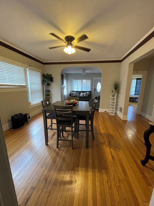 A dining area with a wooden table and chairs, a ceiling fan, and a view into the kitchen. - Historic Home walkable to Top Golf, New Amphitheater, Uptown, City Walk &more! (Birmingham)