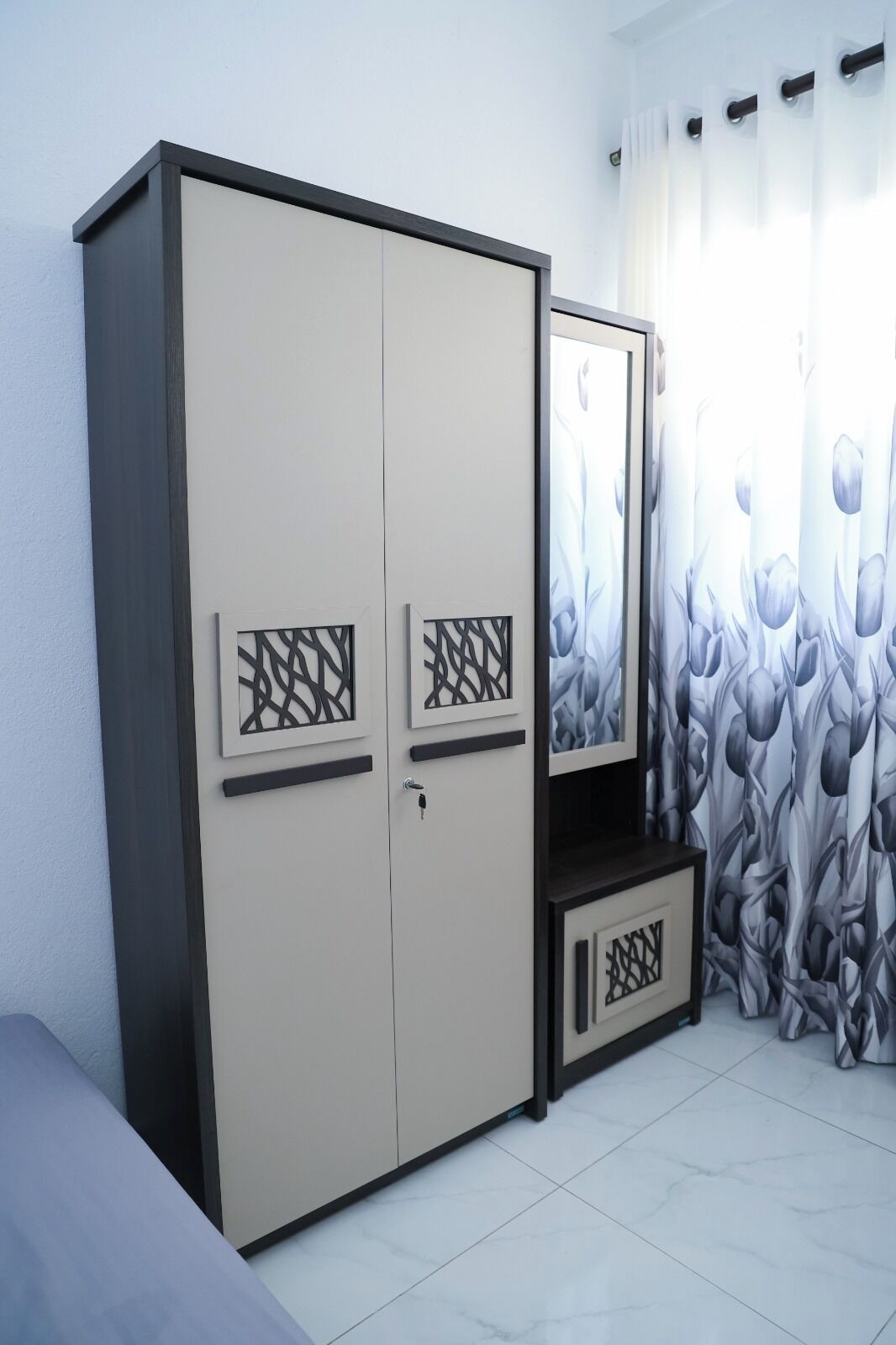A bedroom with a wardrobe, a bed, and a window with curtains.