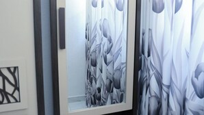 A framed artwork with a floral pattern on a dark wooden stand, positioned above a door with a light-colored wall and a framed abstract design below. - RM Homestay (Negombo)