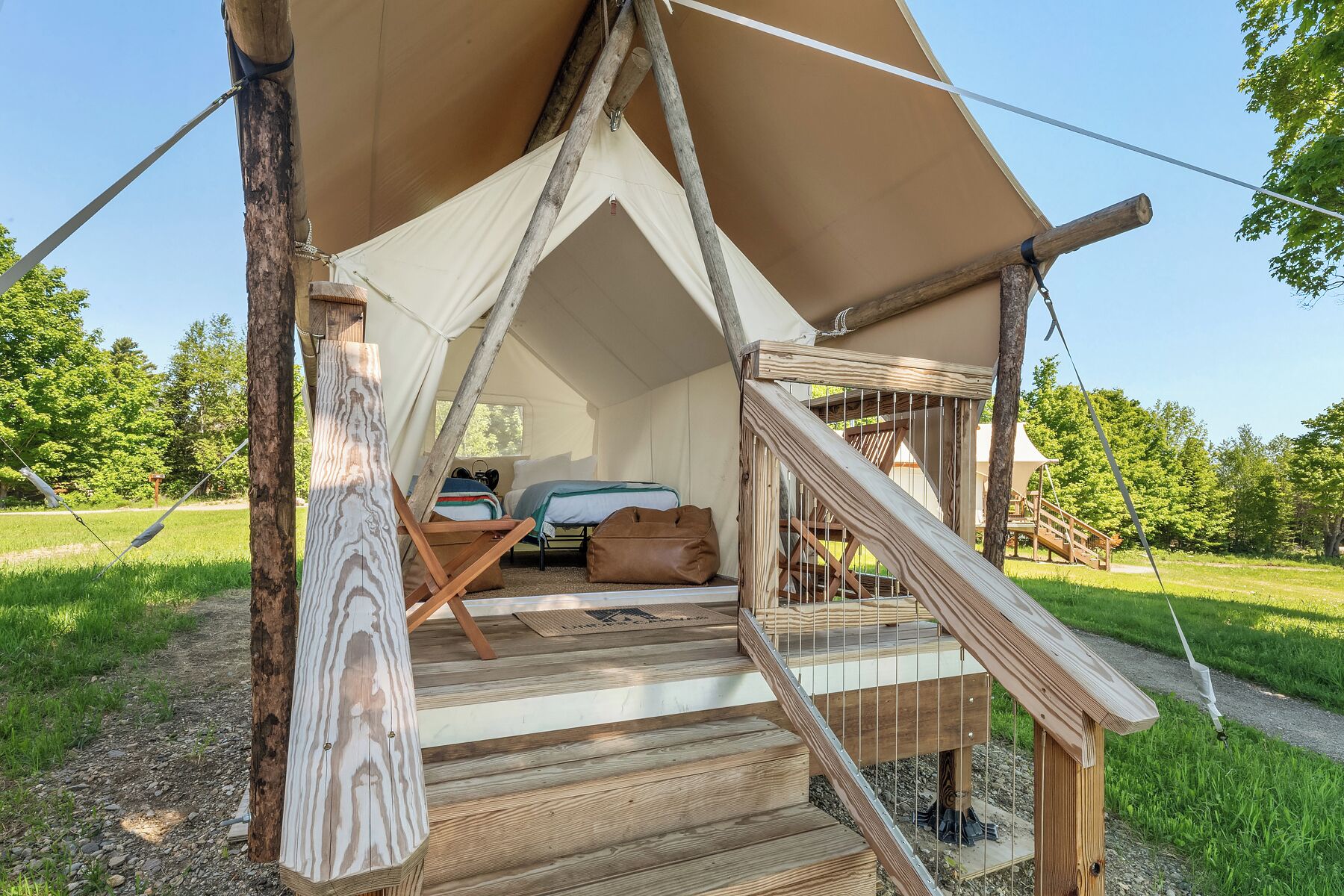 A tent with a bed and a small table, surrounded by a wooden deck and a grassy area.