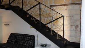 A staircase with a geometric metal railing, a black and white checkered sofa, and a stone wall. - First-floor housing located within the city's Ancient Walls. (Castellammare del Golfo (TP))