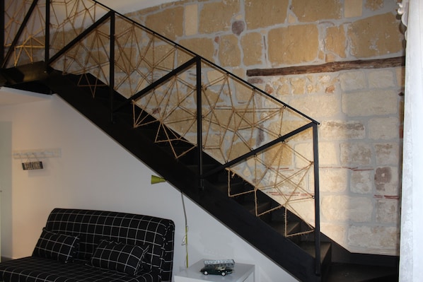 A staircase with a geometric metal railing, a black and white checkered sofa, and a stone wall.