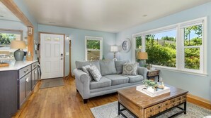A living room with a grey sofa, wooden coffee table, and large windows with a view of greenery. - Beach Glass block from Heart of Saugatuck! (Saugatuck)