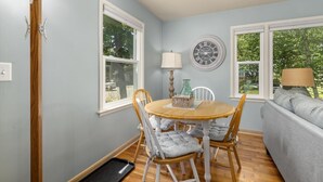 A dining area with a wooden table and chairs, a round clock on the wall, and a sofa in the adjacent living room. - Beach Glass block from Heart of Saugatuck! (Saugatuck)