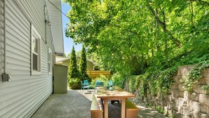 A patio with a wooden table and chairs, surrounded by a stone wall and greenery. - Beach Glass block from Heart of Saugatuck! (Saugatuck)