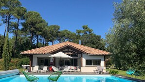 Ein modernes Haus mit Swimmingpool, Sitzgelegenheit im Freien und einem Garten.