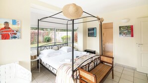 Ein Bett mit Baldachin, ein kleiner Nachttisch, ein Sessel und ein Fenster mit Blick auf Grünflächen.