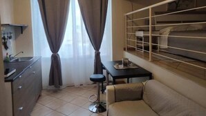 Una habitación compacta con kitchenette, un sofá, una mesita y un televisor fijado en la pared.