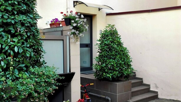 Un patio con suelo de piedra, plantas en macetas, una bicicleta y una escalera que lleva a una puerta.
