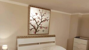 Habitación de hotel con cama, mesita de noche, lámpara, cómoda y un cuadro en la pared.