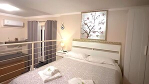 Habitación de hotel con cama, mesita de noche, lámpara, un cuadro y vistas de la ciudad a través de la ventana.