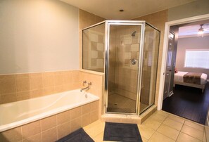 Une salle de bain avec une douche à parois de verre, une baignoire et une porte donnant sur une chambre.