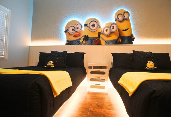 Une chambre d’hôtel avec deux lits, un téléviseur fixé au mur et une décoration sur le thème des Minions.