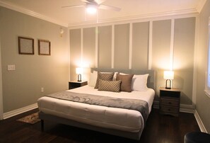 Une chambre avec un grand lit, deux tables de chevet avec des lampes, un ventilateur de plafond et un petit tapis.