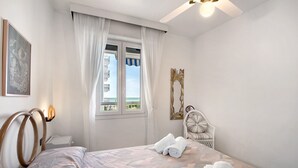 A bedroom with a bed, a nightstand, a chair, a window with curtains, and a ceiling fan.