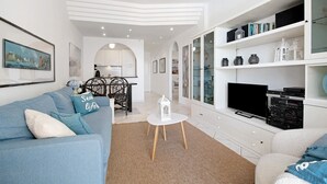 A modern living room with a sofa, a small round table, a television, and a cabinet with shelves.