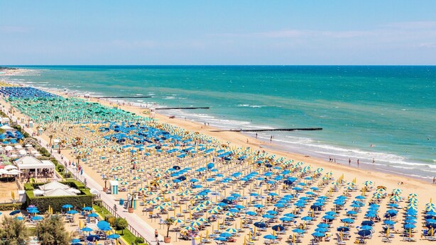 A beach with rows of umbrellas and sun loungers, a clear sky, and the ocean.