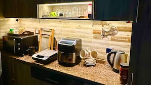 A modern kitchen with a built-in microwave, toaster, and coffee maker. There is a wooden backsplash and a coffee station with cups and a kettle. - The Privacy Villa (6th of October City)
