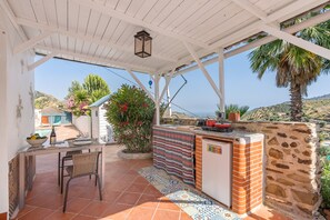 A covered outdoor kitchen area with a table, chairs, and a brick counter.