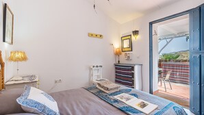 Een slaapkamer met een bed, bedlampje, nachtkastje, dressoir, spiegel, en een open deur naar een balkon met uitzicht.