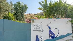 Een muur met een mozaïek van een kat en een hond, omringd door cactussen en andere planten.