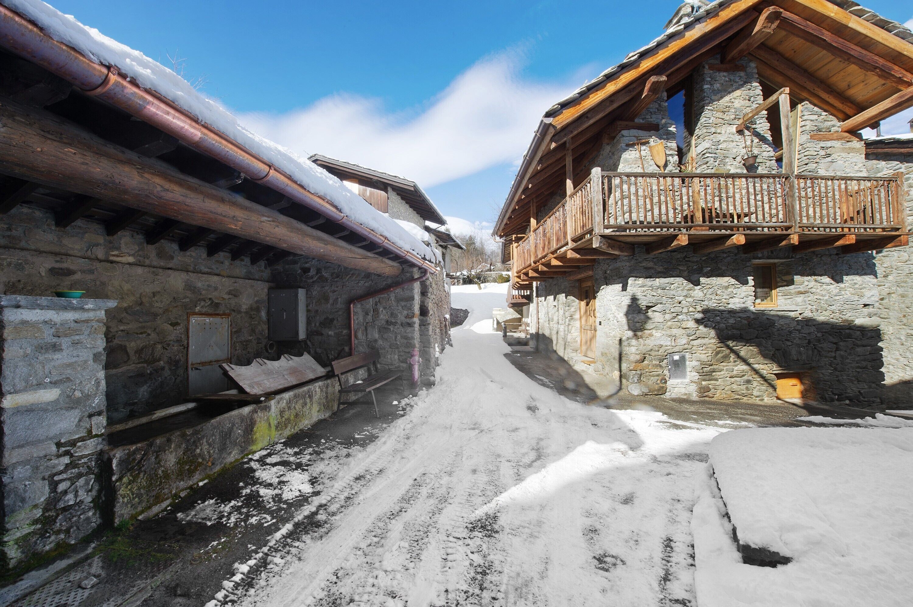 Un sendero estrecho cubierto de nieve flanqueado por edificios de piedra rústicos con balcones de madera.