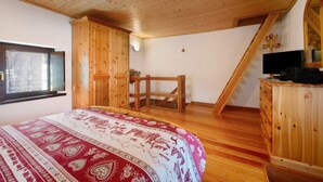 Een slaapkamer met een houten plafond, een bed met een geborduurde spreideken, een houten garderobe en een televisie op een dressoir.