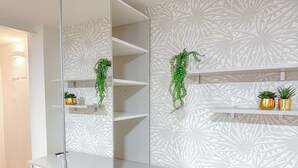 A modern room with a white desk, a chair, and a mirror. There are two shelves with potted plants and a wall with a leaf pattern. - Brunacci Suite - 5 min dai Navigli (Milano)