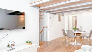 A modern living room with a flat-screen TV, a white console table, and a dining area with a round table and chairs. - Brunacci Suite - 5 min dai Navigli (Milano)