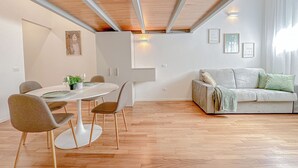 A modern living space with a dining area, a sofa, and a ceiling with exposed beams. - Brunacci Suite - 5 min dai Navigli (Milano)