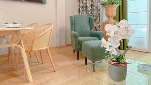 A modern living room with a dining area, a green armchair, wicker chairs, and a glass coffee table with a potted orchid. - Cirillo Luxury Suite 16 - Arco della Pace (Milano)