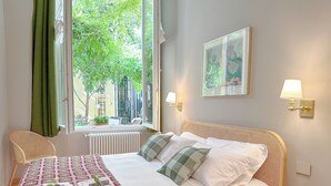 A neatly made bed with a checkered blanket, a chair, a bedside table with a lamp, and a window with curtains. - Cirillo Luxury Suite 16 - Arco della Pace (Milano)