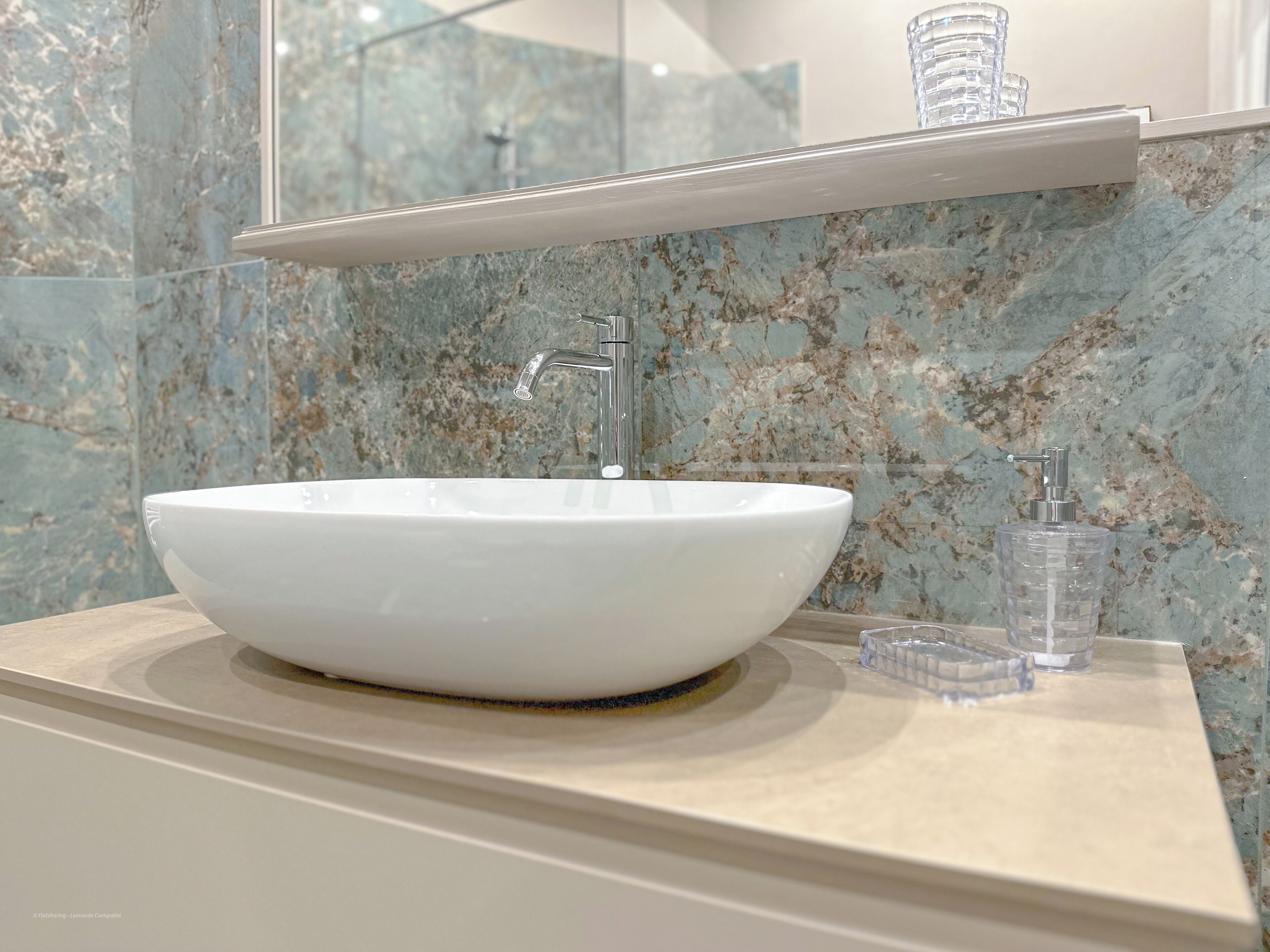 A bathroom with a white vessel sink, a faucet, and a soap dispenser on a marble countertop.
