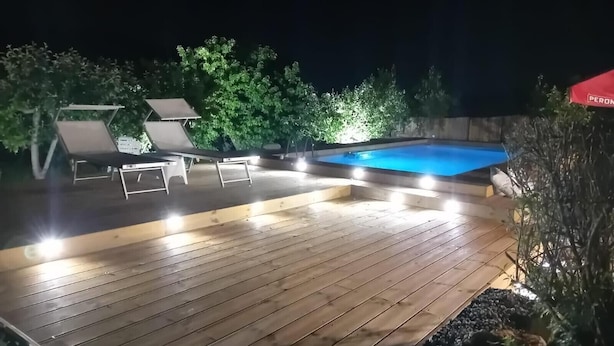 A wooden deck with a swimming pool, lounge chairs, and a red canopy.