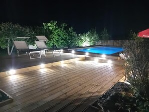 A wooden deck with a swimming pool, lounge chairs, and a red canopy.